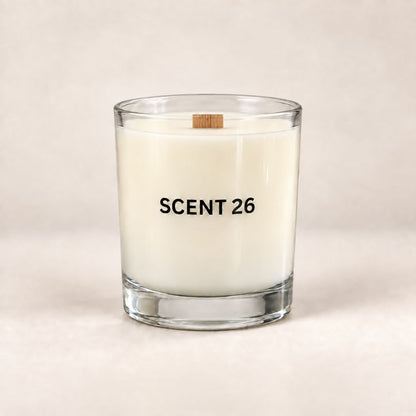 A clear glass jar candle with white wax and a small wooden wick, printed with the text 'SCENT 26' in black, set against a neutral beige background.