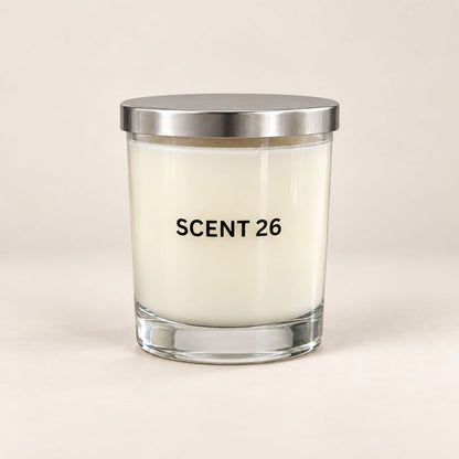 A glass jar candle with off-white wax and a brushed silver metal lid, featuring the text 'SCENT 26' printed in black on the front, set against a solid light beige background.