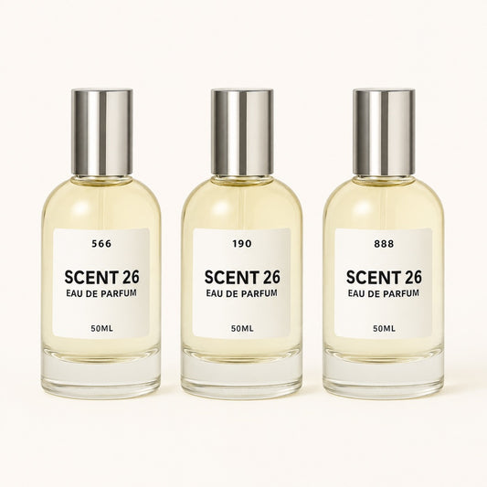 Three identical 50ml bottles of Scent 26 Eau De Parfum arranged side by side on a clean off-white background. Each bottle has a clear glass body filled with pale yellow liquid, a white label with black text, and a reflective silver cap.