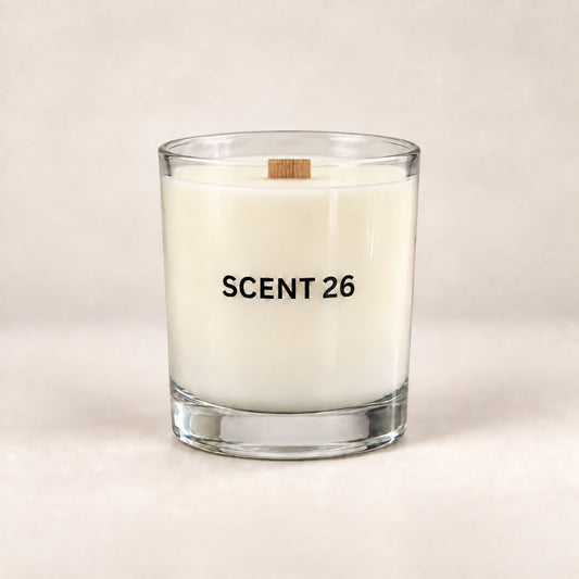 A clear glass jar candle with white wax and a small wooden wick, printed with the text 'SCENT 26' in black, set against a neutral beige background.