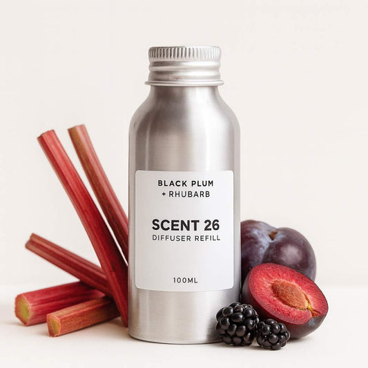 Scent 26 Black Plum + Rhubarb diffuser refill 100ml bottle surrounded by rhubarb stalks, plum halves and blackberries, highlighting a juicy fruity fragrance with tart sweetness